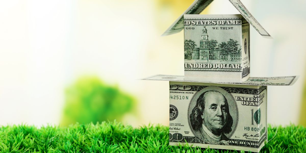 House made from hundred-dollar bills on a grass surface.