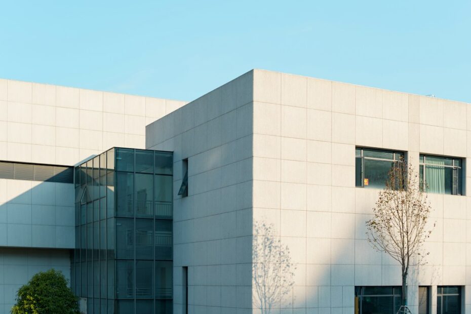 Real estate professional in business attire stands outside a modern glass commercial building, analyzing data on a tablet.